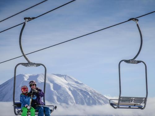 Krista Crabtree and her daughter ride a chairlift with Japan's Mt. Yotei volcano in the background.