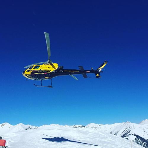 The Silverton Mountain helicopter flies with blue ski background.