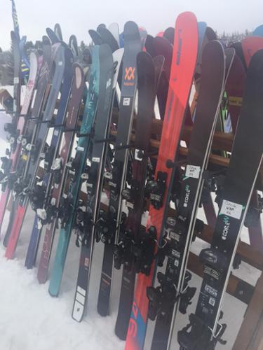 A dozen Elan skis sit in a rack waiting to be skied on.